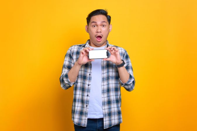 Surprised Asian male holding smart phone showing blank screen
