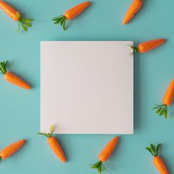 Easter pattern made with carrots on bright blue background with paper card