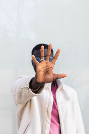 Black man covering face and showing stop gesture in city street
