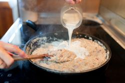 Person adding milk to the croquette dough in a pan