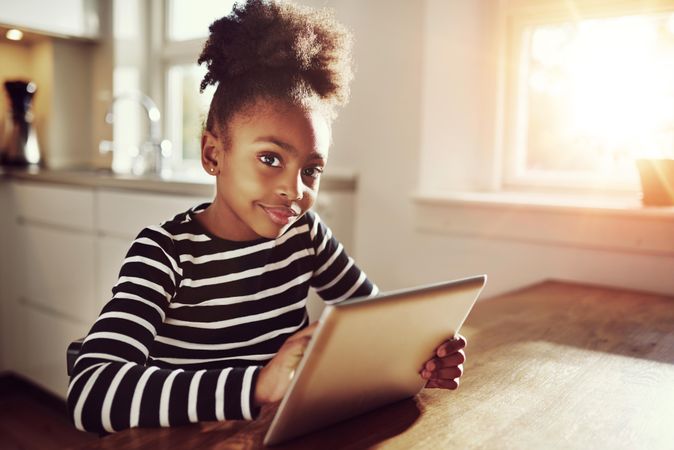 Shot of girl looking at camera in sunny room with tablet in hand