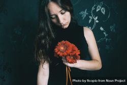 Studio portrait of woman with holding gerbera flowers against floral wall 4mBZBb