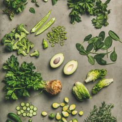 Arrangement of fresh green sliced garden vegetables on concrete surface, square crop