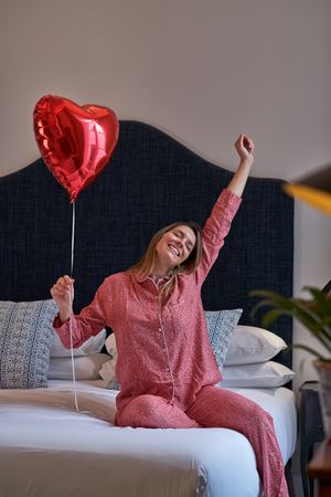 Dreaming woman with red heart balloon sitting on bed