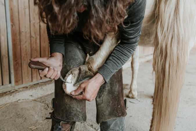 Man shoeing horse near stable