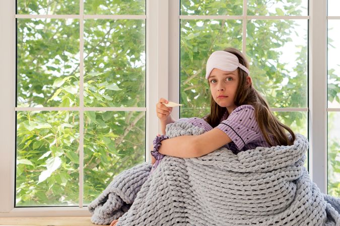 Girl holding an electronic thermometer, looking thoughtful