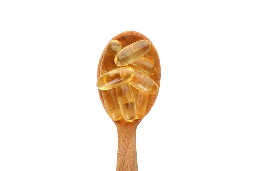 Wooden spoon with omega pills, isolated on blank background