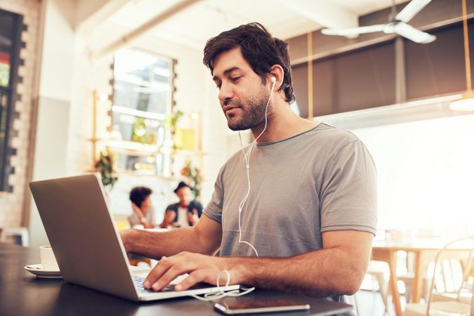 Portrait of a young man with earphones using laptop at a cafe