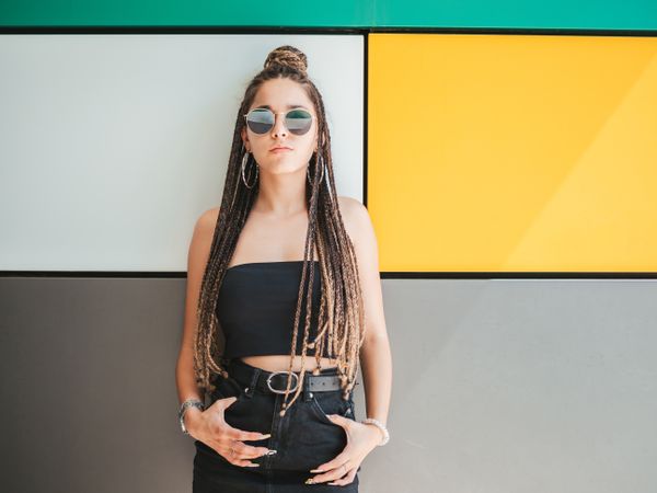 Charming teenage girl with dreadlocks in sunglasses nearby colorful wall