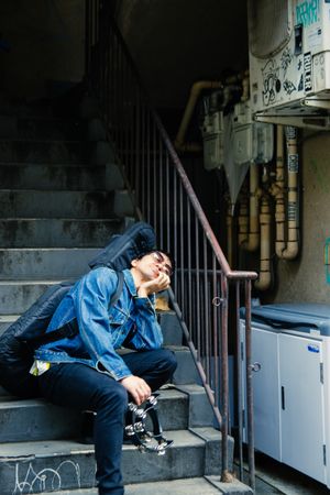 Man in denim jacket holding a guitar in a bag sitting out