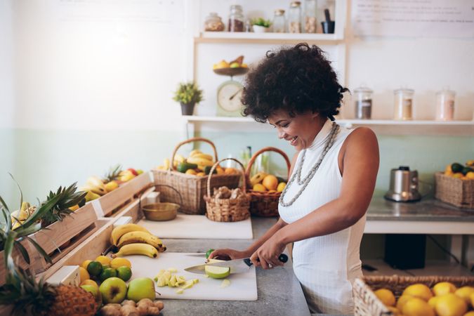 Young woman working at juice bar and cutting fruits