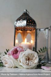 Silver Moroccan, Arabic lantern with burning candle. Pink roses flowers on table. Festive still life for muslim holiday Ramadan Kareem or boho wedding. Blurred background, vertical. beXO9l