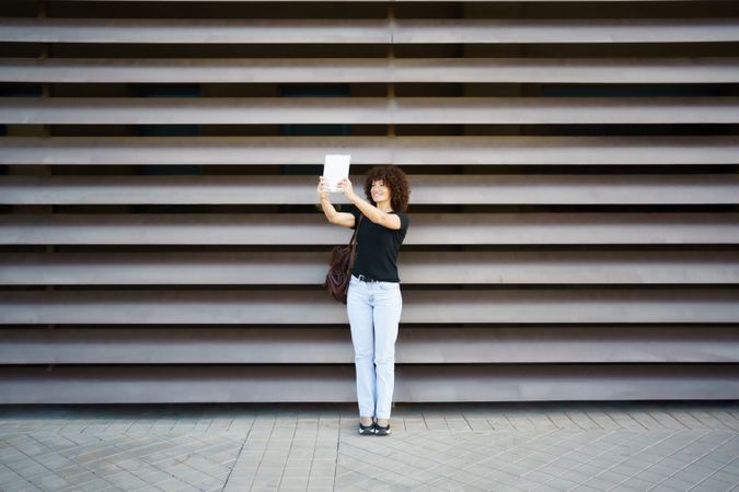 A Cheerful Woman Taking a Fun Selfie Against a Modern Textured Wall with a Big Smile