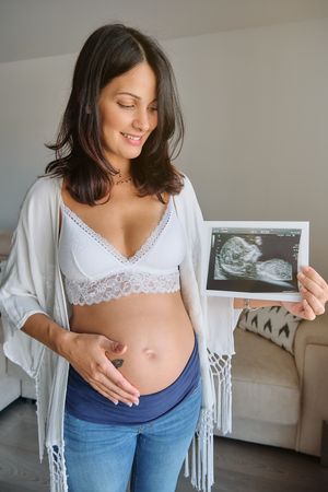 Happy pregnant lady with ultrasound image at home