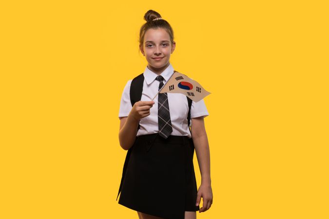 Schoolgirl holds South Korean flag while smiling confidently.