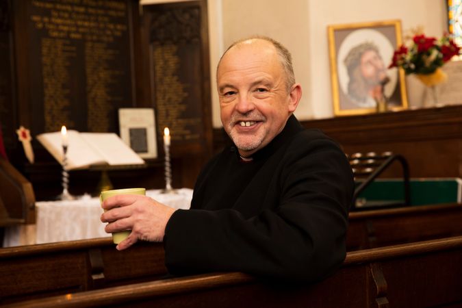 Vicar with cup of tea in pews