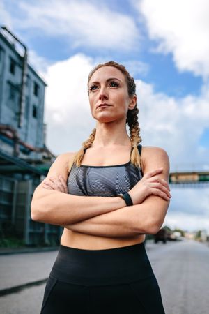 Sporty woman with crossed arms posing in front of a factory