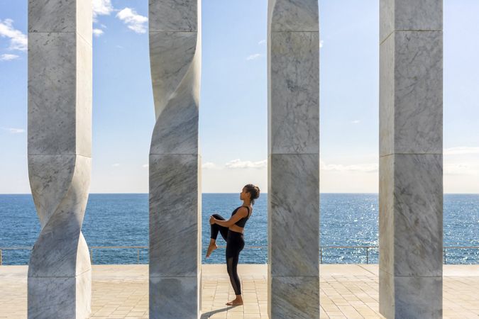 Side view of female doing yoga between sculpture by the ocean