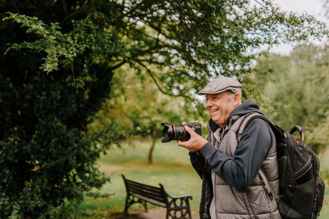 Older man with large camera next to trees in a park