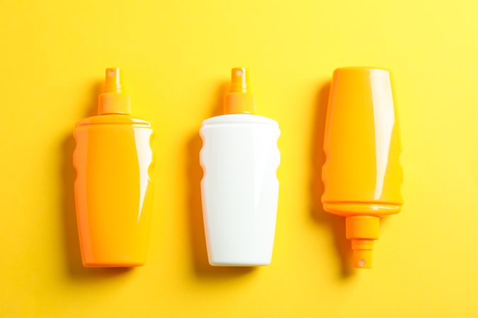 Flat lay composition with sunscreen sprays on color background, top view, closeup. Summer vacation