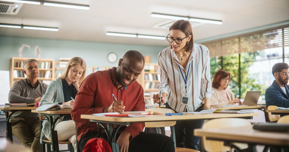 Young Teacher Checking Up on a Black Male, Helping Him with a School Task, Complimenting His Work.