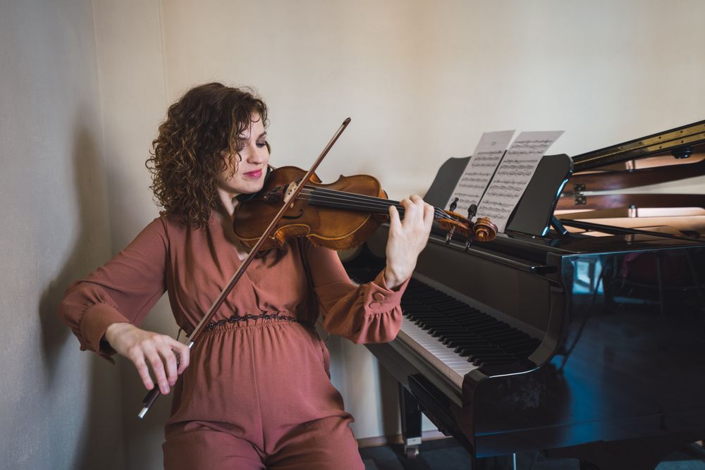 Pregnant woman playing on violin near piano in room