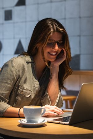 Smiling woman surfing internet on laptop at cafe table