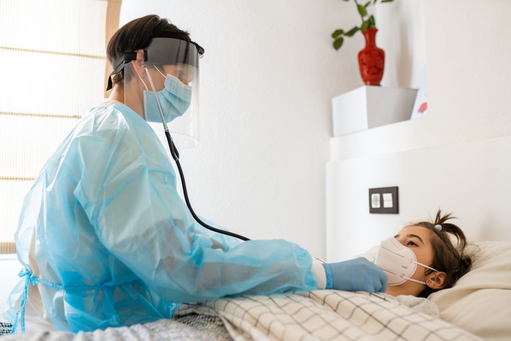 Doctor with facemask using stethoscope on a patient in bed