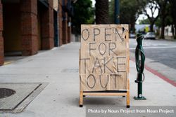 Sandwich board on city sidewalk with “open for takeout” hand lettered 4BapM5