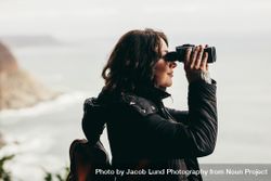 Woman wearing warm jacket looking through binoculars 5qomab