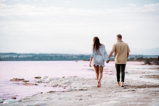 back view of adorable couple walking on an amazing beach with pink water