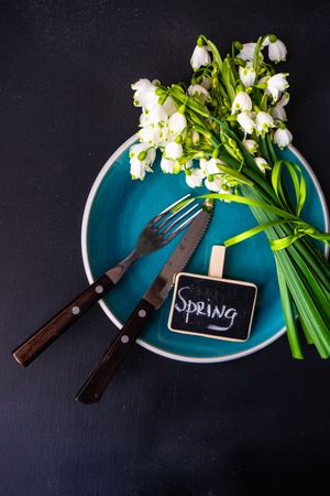 Top view of table setting for spring dinner with flowers on teal plate