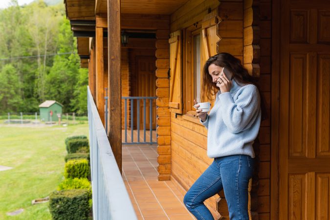 Content woman talking on smartphone on terrace of house