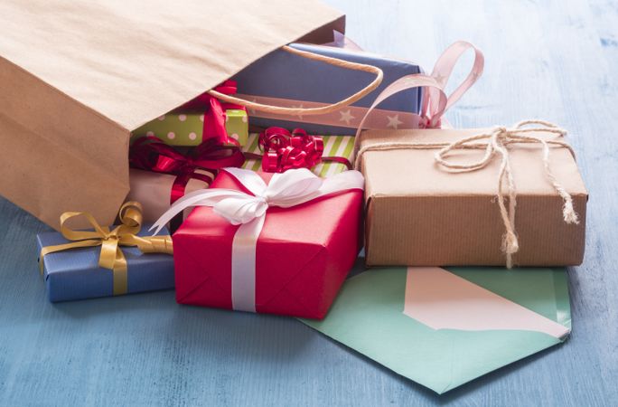 Colorful presents falling out of brown paper bag on blue table