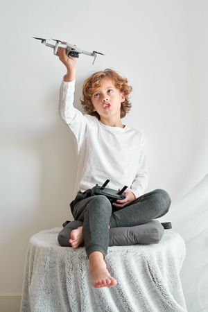 Child playing with toy drone on table near wall