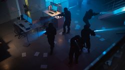 Masked Squad of Armed SWAT Police Officers Storm a Dark Seized Office Building with Desks and Computers.