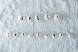 Wooden table background with snow and lights ball decoration reading “Merry Christmas”
