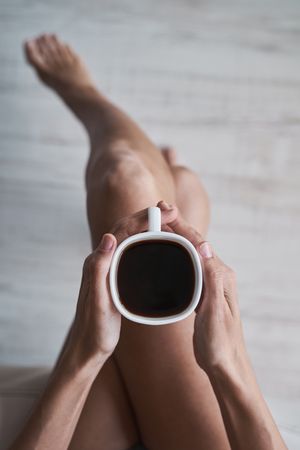 Faceless woman sitting with coffee cup in hands