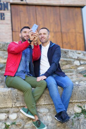 Cute male couple taking selfie sitting on rock wall