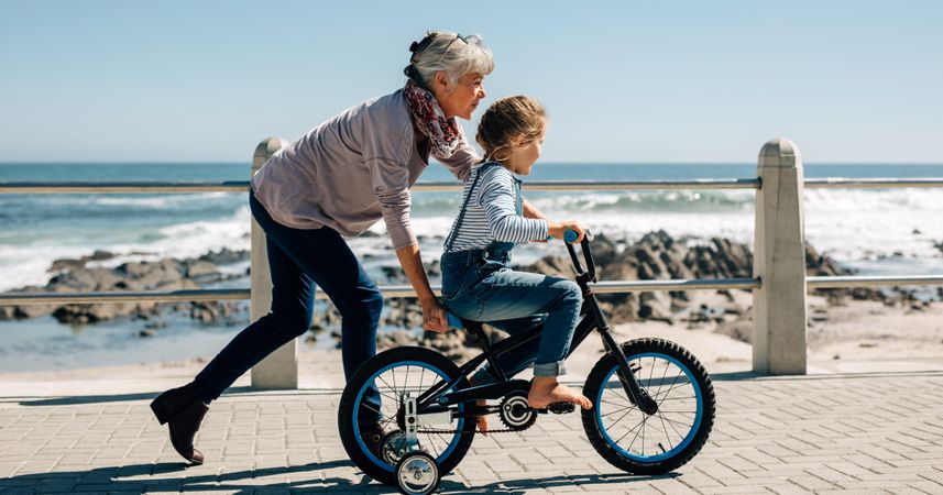 Side view of a girl riding a bicycle while her grandmother runs along holding the kid