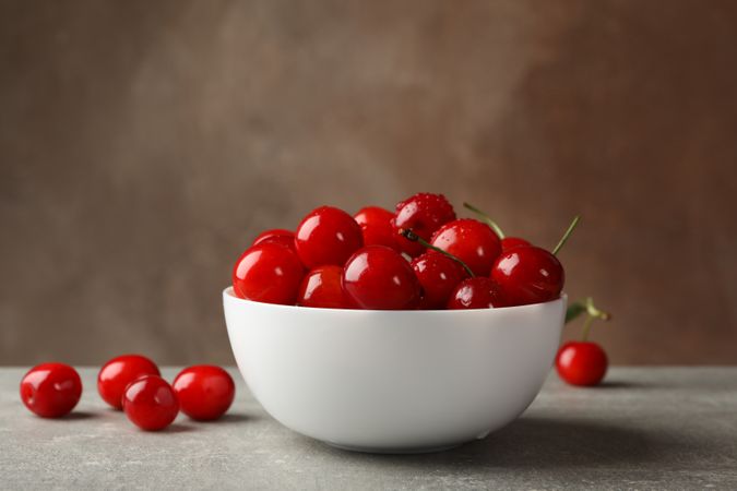 Bowl with red cherry on gray table, space for text