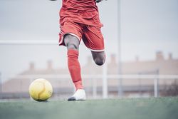 Black soccer player with red outfit playing soccer.