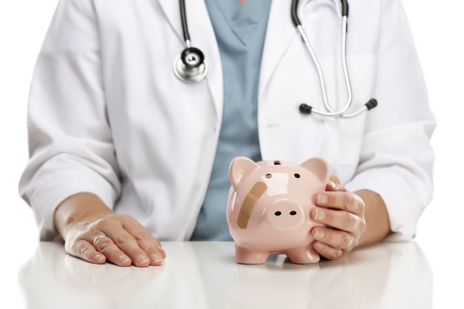Doctor Holding Caring Hand on a Piggy Bank with Bandage