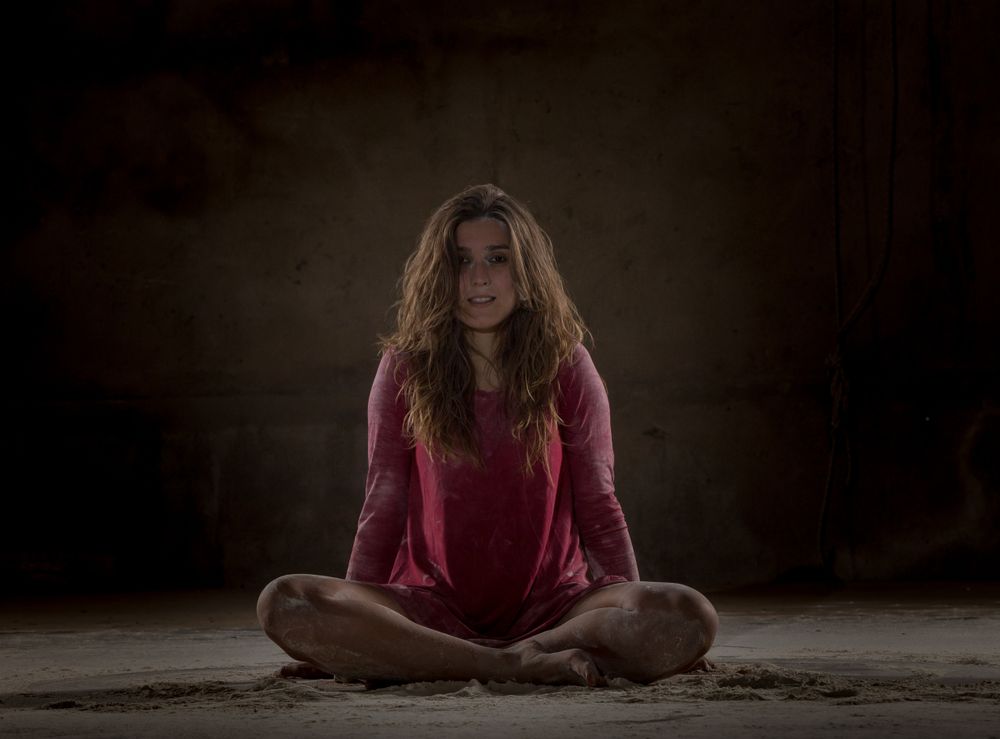Young woman in lotus pose between sand in darkness