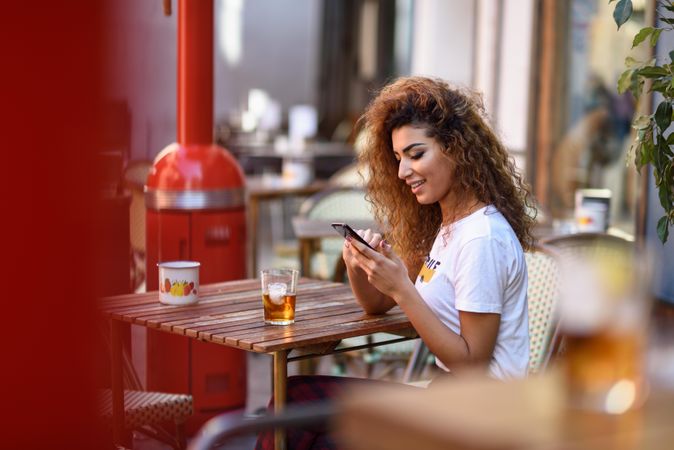 Arab woman in casual clothes checking her phone on cafe patio
