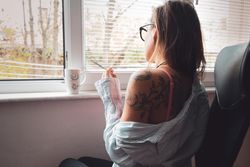Woman smoking by the window with a cup of tea