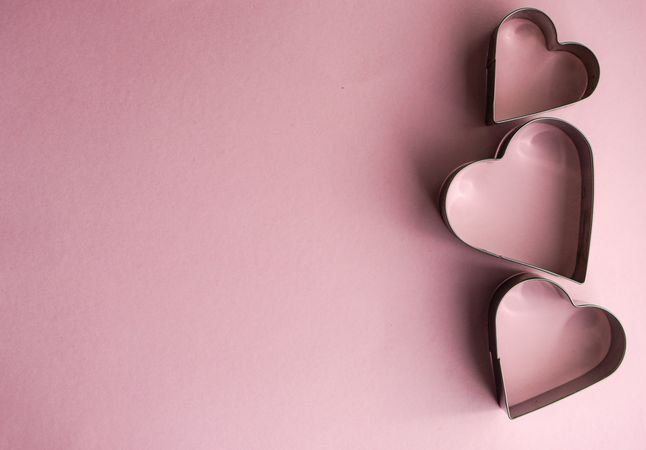 Three heart shaped cookie cutters on pink background with space for text