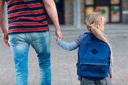 Back view of father holding the hand of his daughter who is going to school