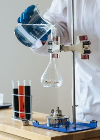 Cropped image of person pouring liquid into heated flask in chemistry lab