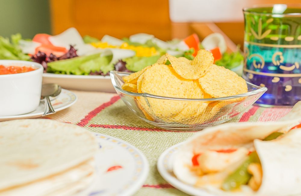Traditional mexican food with a bowl of nachos, spicy sauce, a plate of chicken fajita, tortillas and fresh salad